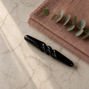 The Obsidian Bar on a marble bathroom shelf beside a folded dusty-rose towel and eucalyptus
